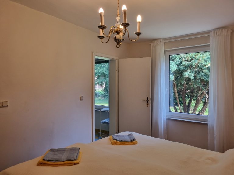 Schlafzimmer 1 mit Tür zum Bad und Fenstern in den Vorgarten.